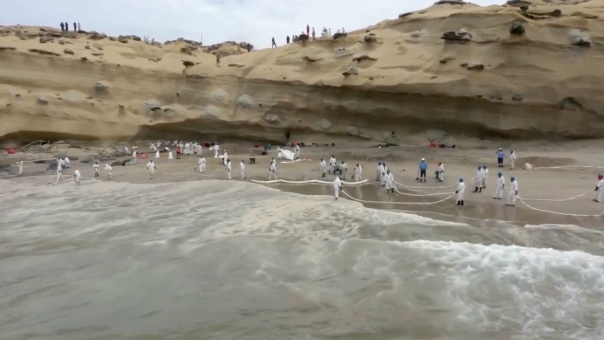 Emergency workers try to contain an oil spill on a beach in Peru