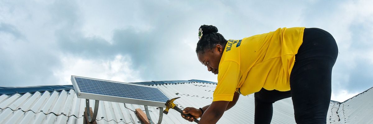 Eposi Njoh Monyengi fixes a solar panel on the roof of a house in Tiko, Cameroon on May 24, 2022.