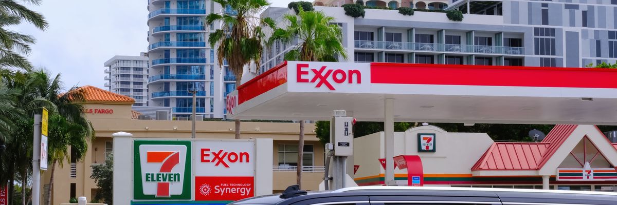 Exxon gas station with 7-Eleven branding is seen against modern high-rise buildings, palm trees, and a passing black SUV.