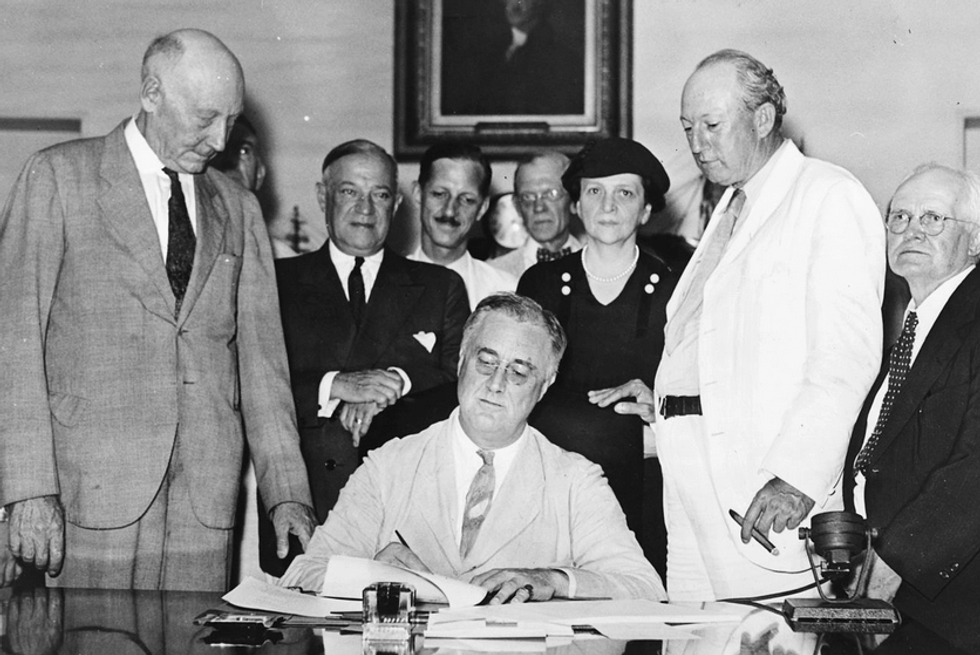 FDR signs Social Security legislation with Frances Perkins perched over his left shoulder.