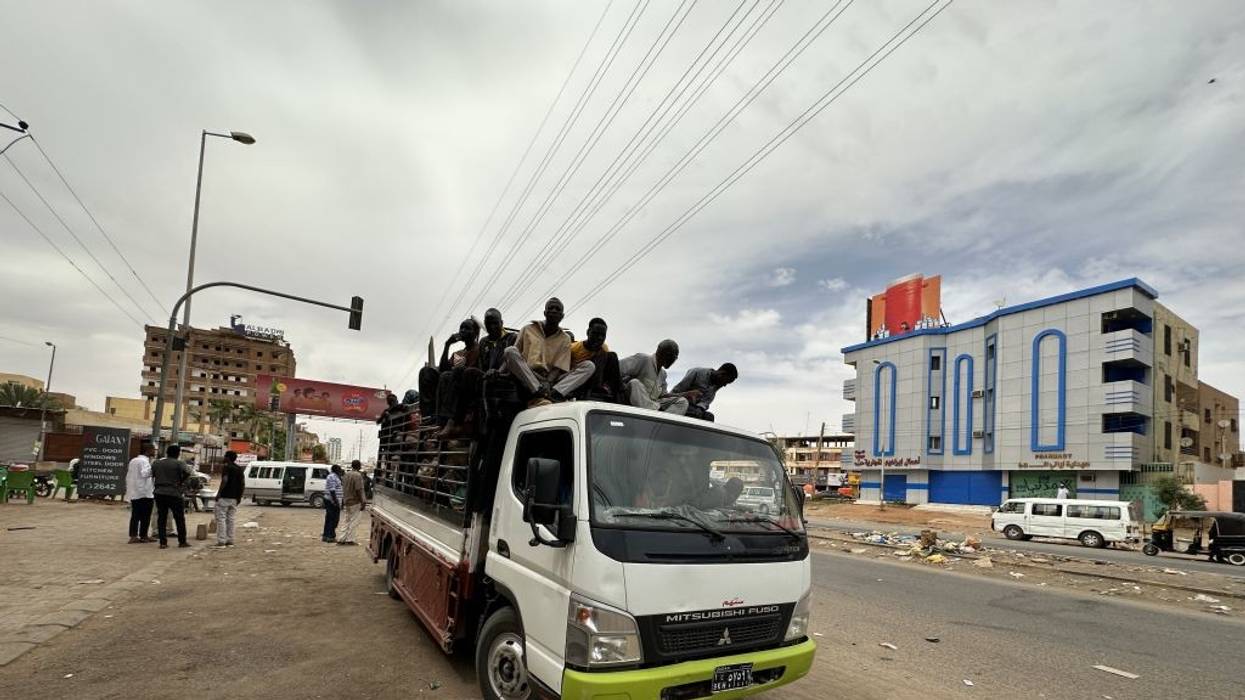 Figures ride on top of a van down a litter-strewn street.