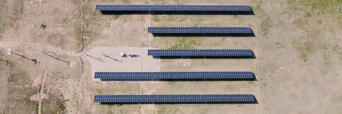Five rows of solar panels over parched ground.