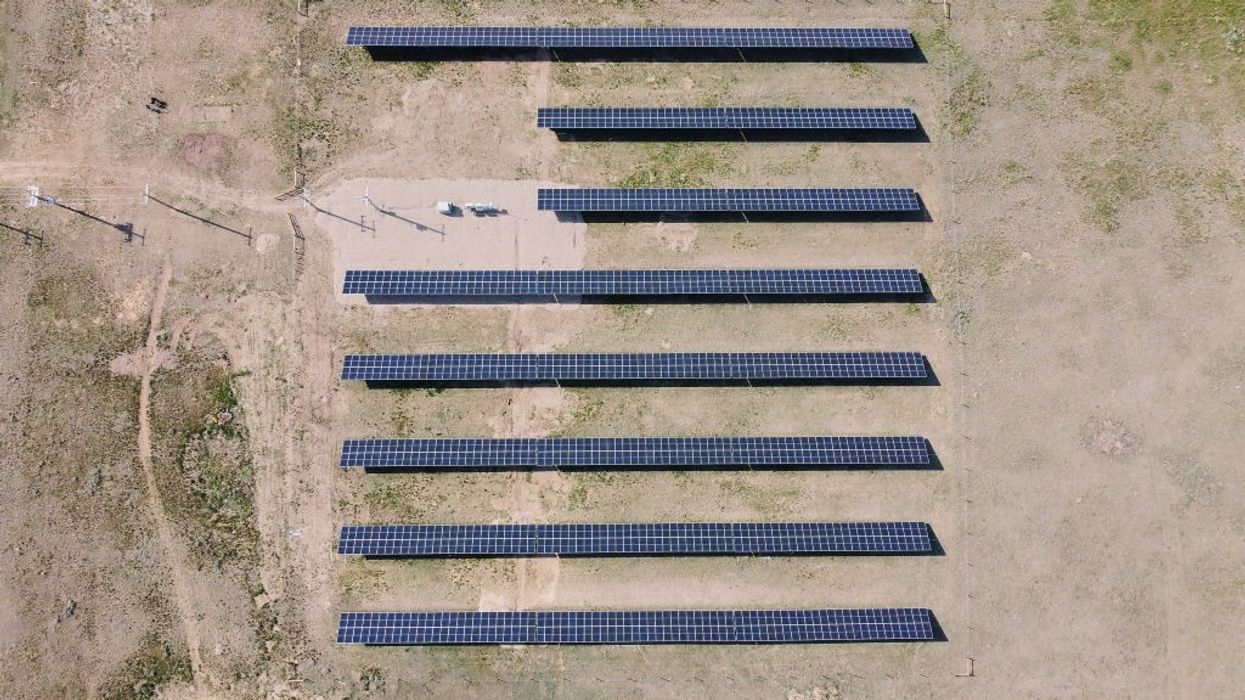 Five rows of solar panels over parched ground.