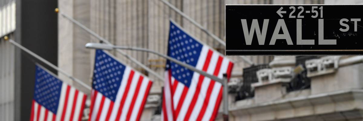 Flags fly in front of the New York Stock Exchange behind a Wall Street sign.