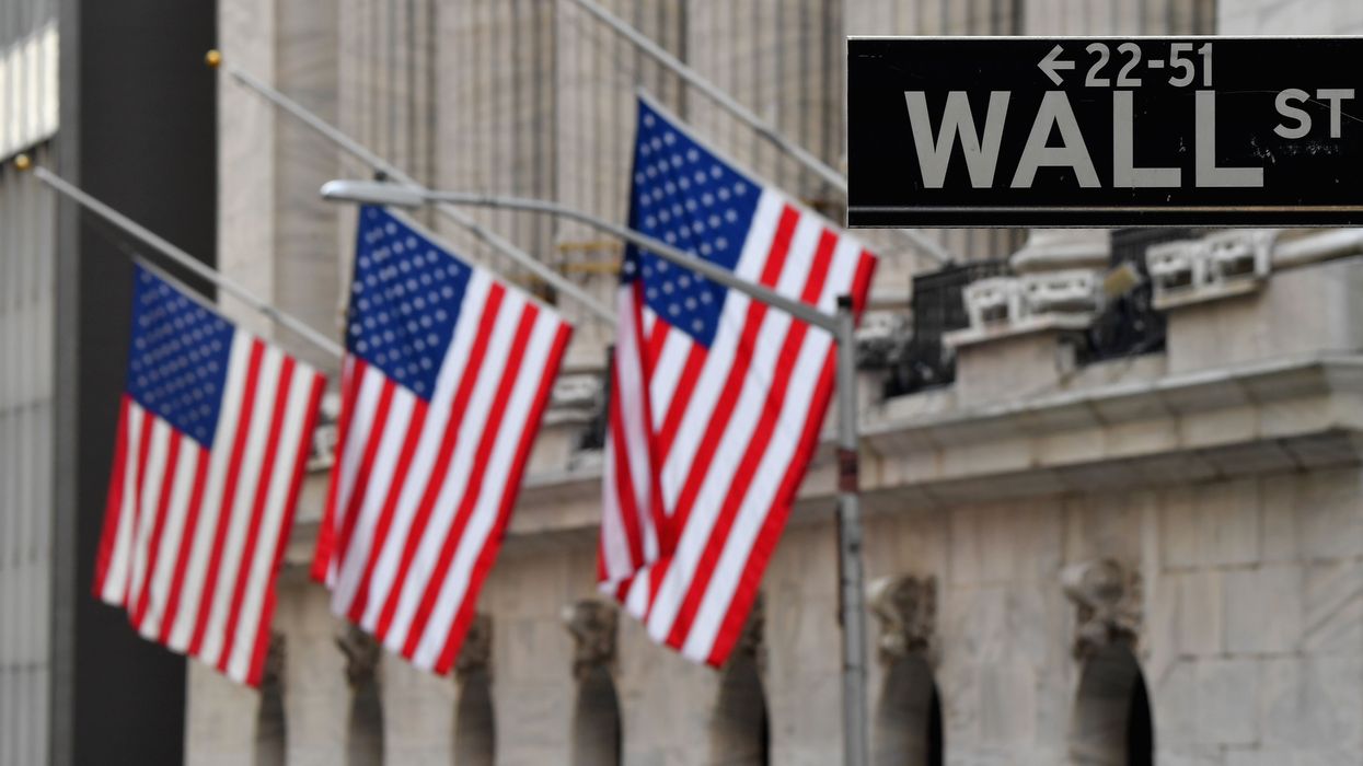 Flags fly in front of the New York Stock Exchange behind a Wall Street sign.