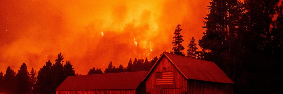 Flames rip across a hillside behind a building donning a U.S. flag as the Caldor Fire pushes into South Lake Tahoe, California on August 30, 2021. (Photo: Josh Edelson/AFP via Getty Images)