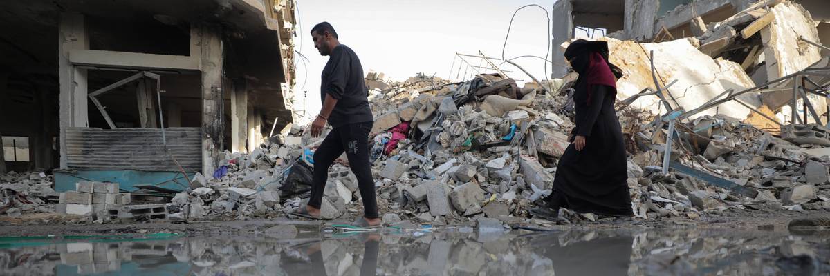 Gazans, including children, walk past rubble and leaked sewage