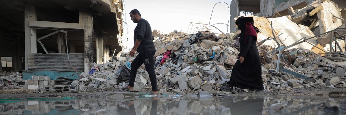 Gazans, including children, walk past rubble and leaked sewage