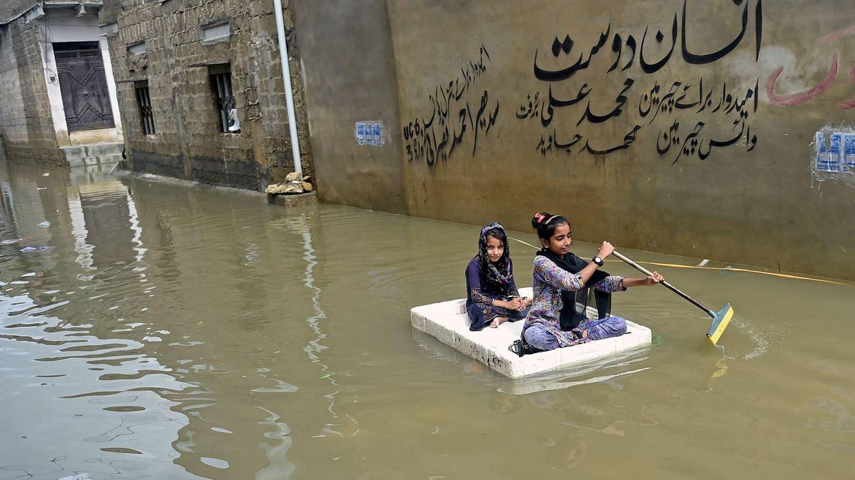 Girls use a temporary raft across a flooded street in a residential area after heavy monsoon rains in Karachi on July 26, 2022