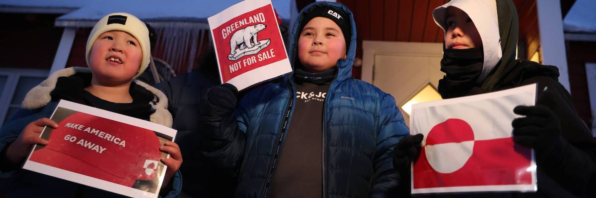 Greenland children hold signs reading "Make America Go Away" and "Greenand Not for Sale"