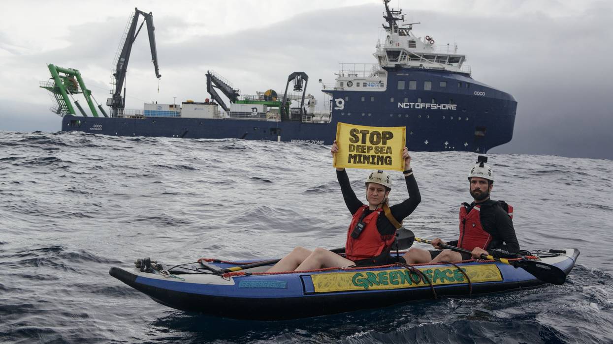Greenpeace kayaktivists hold up a sign reading "stop deep sea mining" near an exploration ship