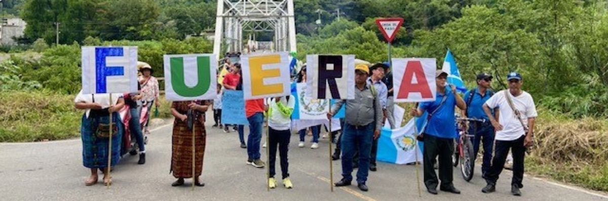 Guatemalan protesters stand on a road with letters spelling out "Fuera," or "Out."