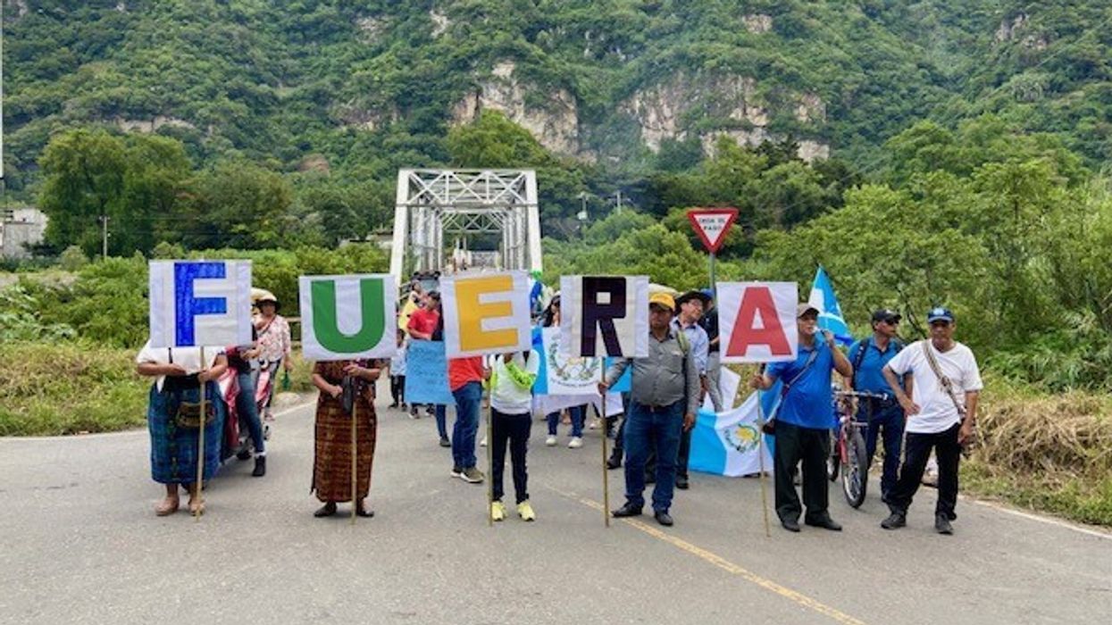 Guatemalan protesters stand on a road with letters spelling out "Fuera," or "Out."