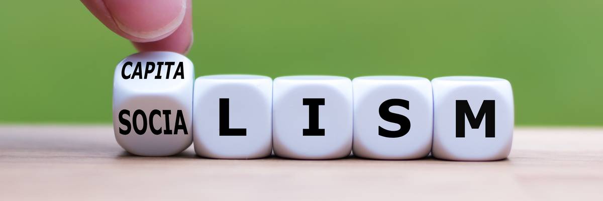Hand flips a dice and changes the word "Socialism" to "Capitalism", or vice versa.