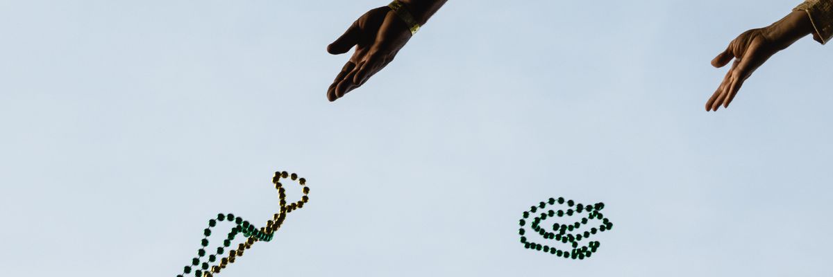 Hands toss Mardi Gras beads into the air.