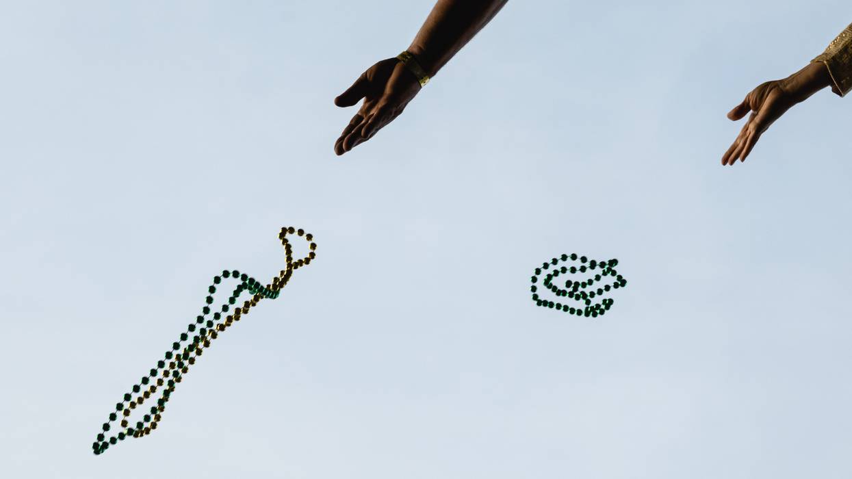 Hands toss Mardi Gras beads into the air.