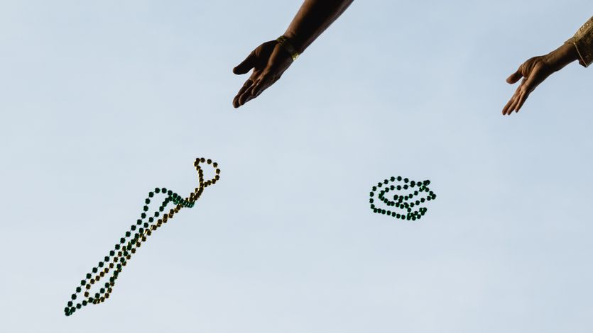 Hands toss Mardi Gras beads into the air.