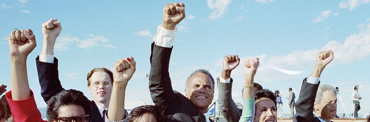 Harry Belafonte stands in the center of a crowd raising fists.