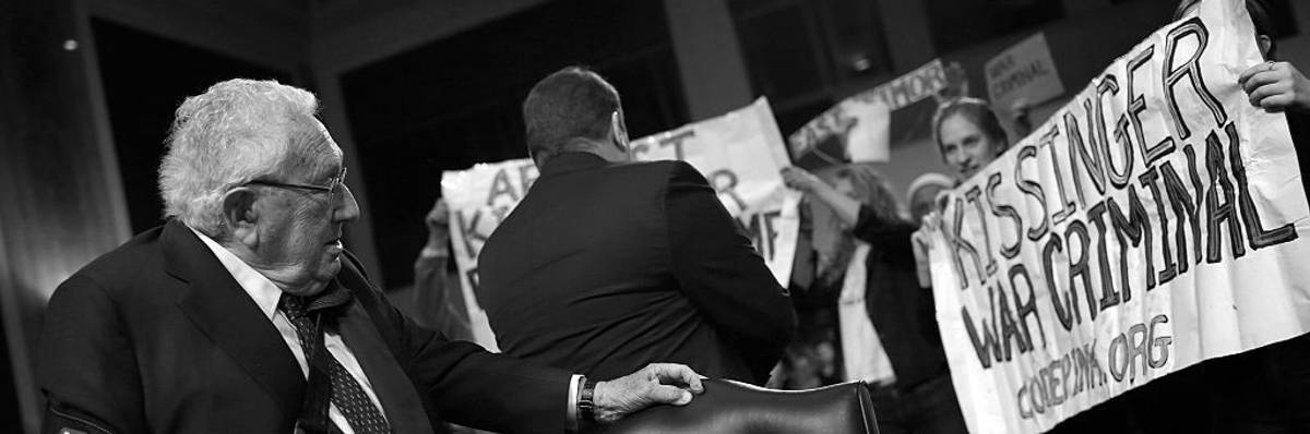 Henry Kessinger confronted by a sign reading, "Kissinger: War Criminal"