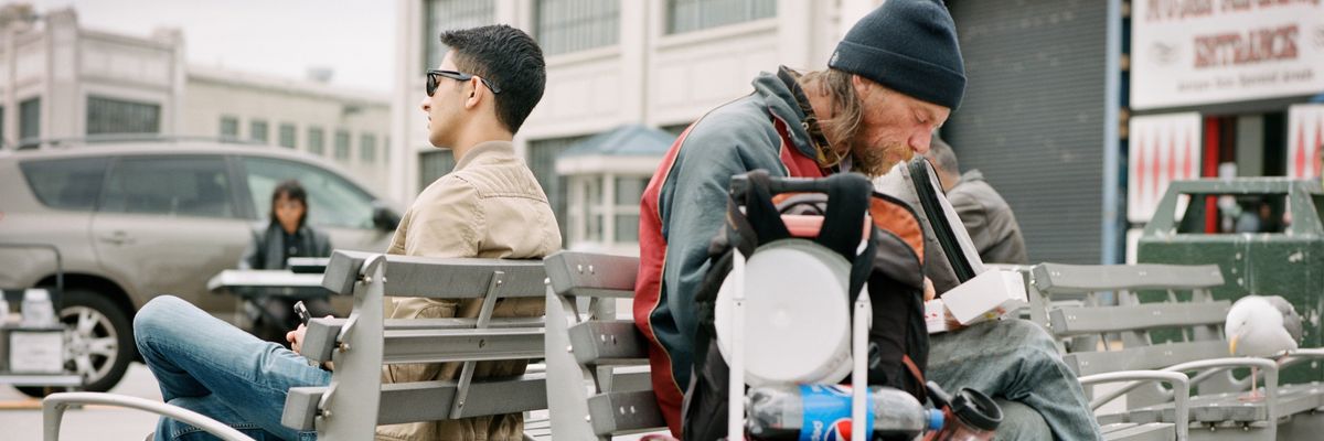 Homeless man on a bench with back to another man nicely dressed
