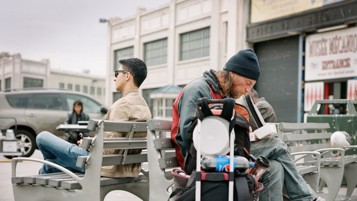 Homeless man on a bench with back to another man nicely dressed