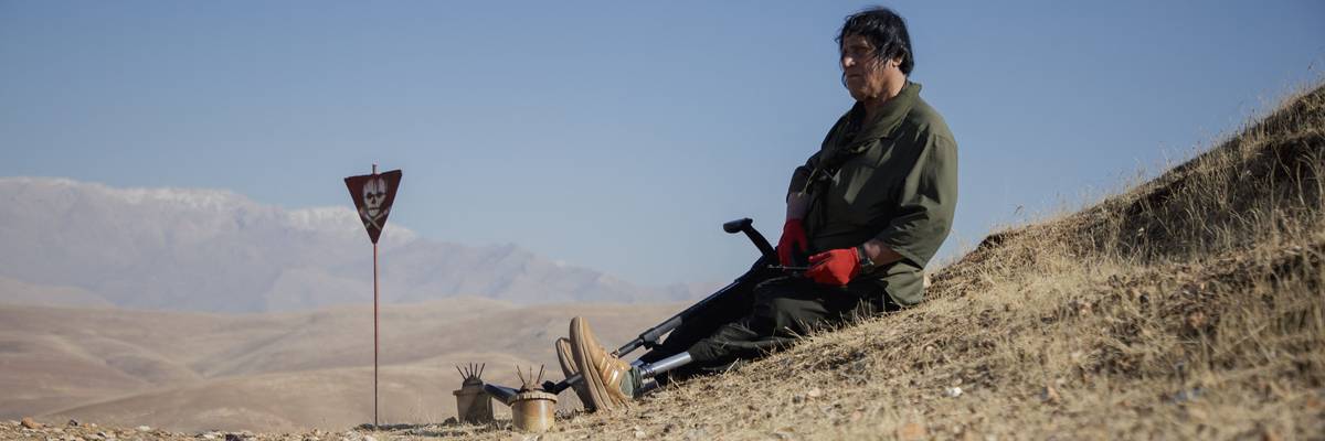 Hoshyar Ali, who lost both legs and several family members to explosions, sits near landmines on a hillside in Halabja, Iraq