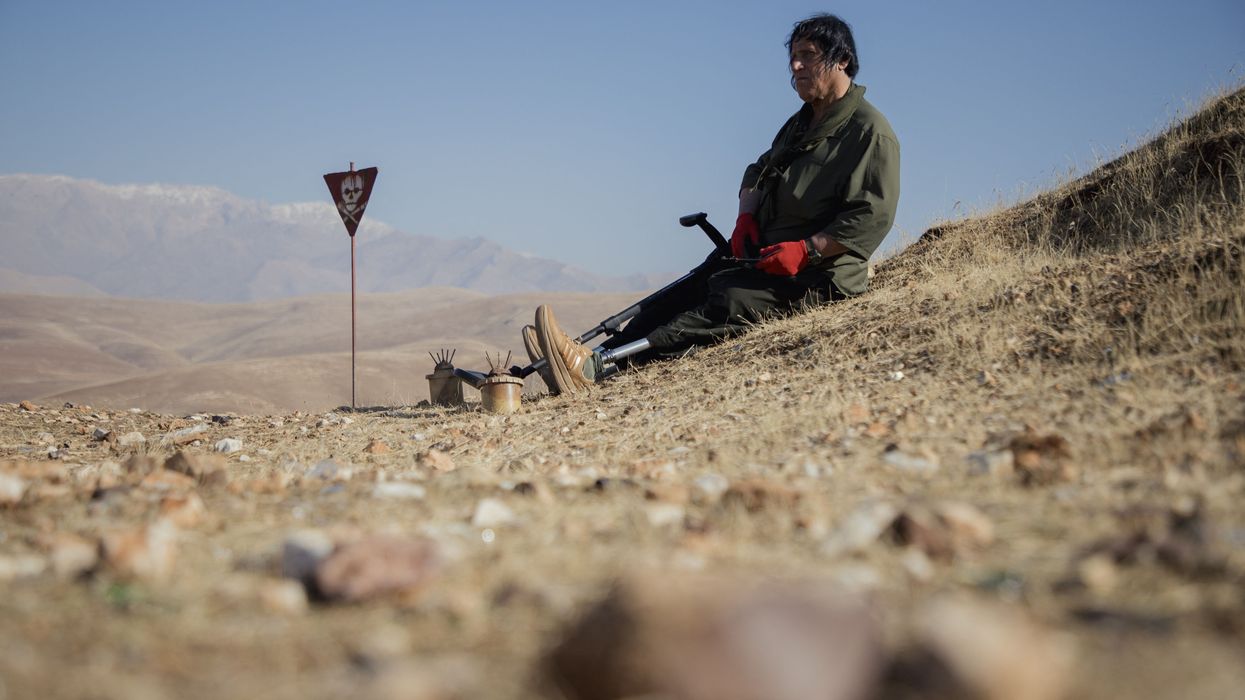 Hoshyar Ali, who lost both legs and several family members to explosions, sits near landmines on a hillside in Halabja, Iraq