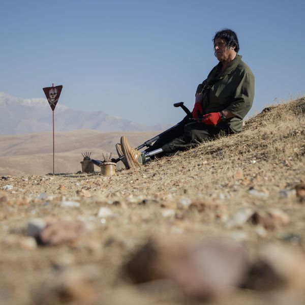 Hoshyar Ali, who lost both legs and several family members to explosions, sits near landmines on a hillside in Halabja, Iraq