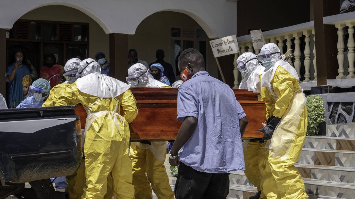 Hospital workers in protective gear move a coffin of a suspected Ebola victim