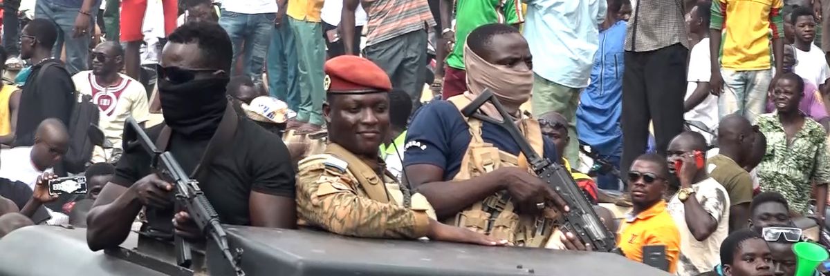 Ibrahim Traoré rides in a vehicle with crowds behind him.