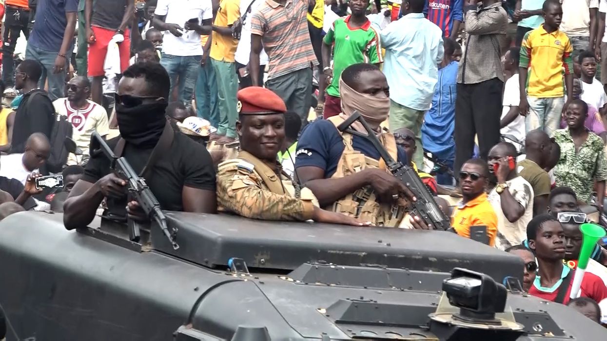 Ibrahim Traoré rides in a vehicle with crowds behind him.