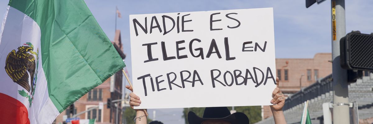 Immigrants' rights protester holds up sign saying, "No one is illegal on stolen land" in Spanish.