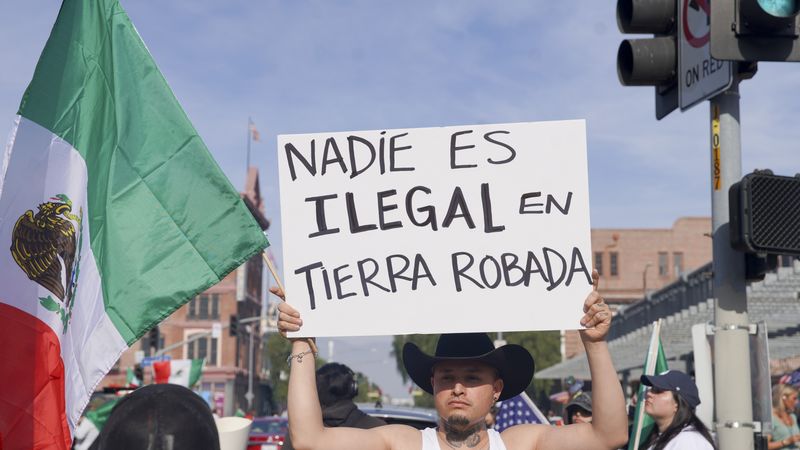 Immigrants' rights protester holds up sign saying, "No one is illegal on stolen land" in Spanish.