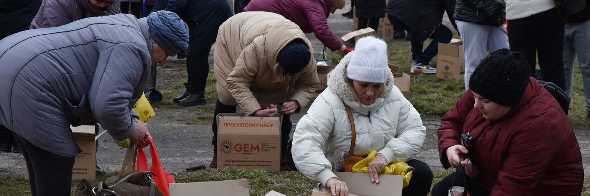 Internally displaced people open boxes of supplies in Ukraine while wearing parkas.