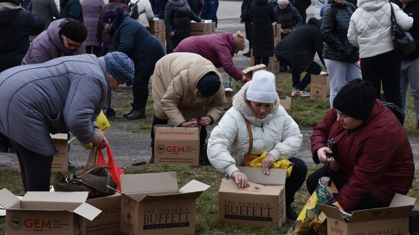 Internally displaced people open boxes of supplies in Ukraine while wearing parkas.