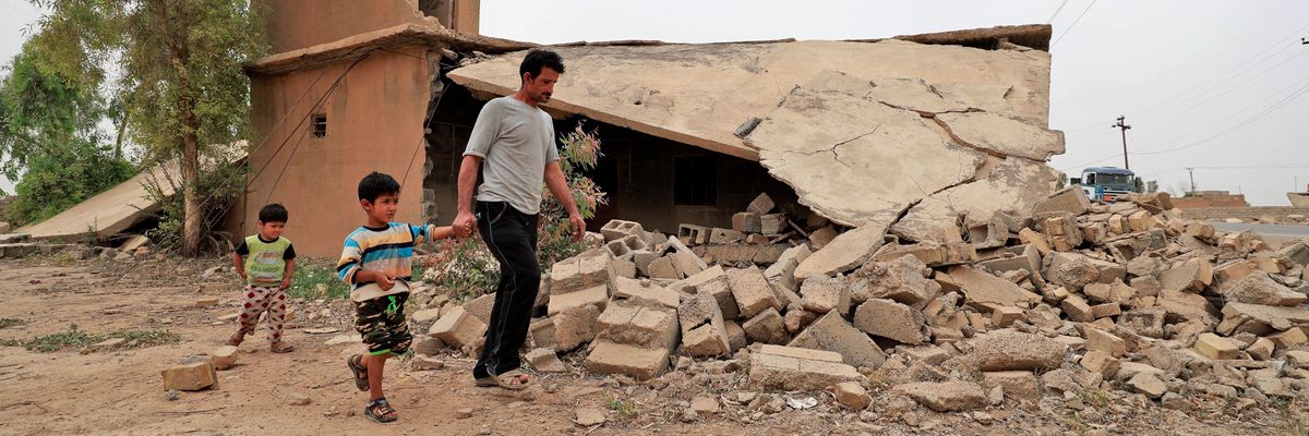 Iraqi father and children walk past a destroyed house