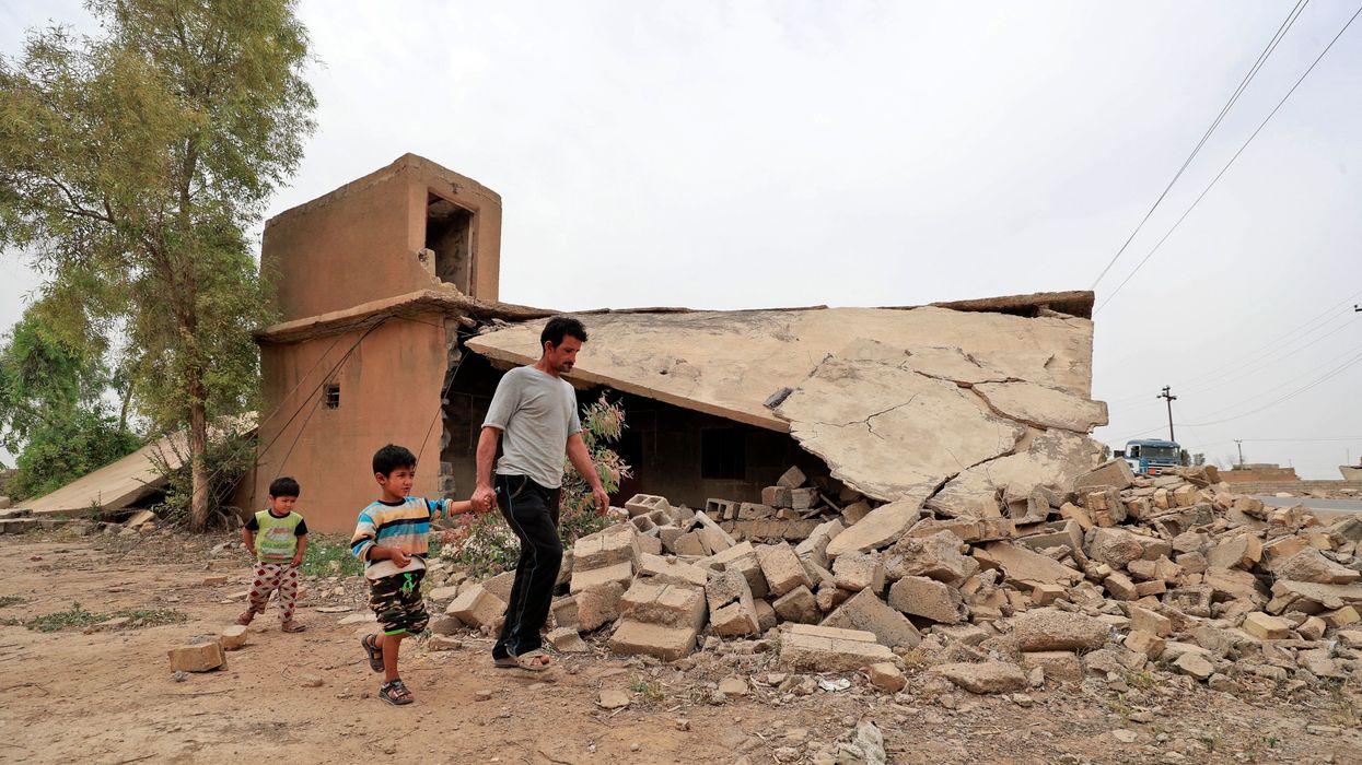Iraqi father and children walk past a destroyed house