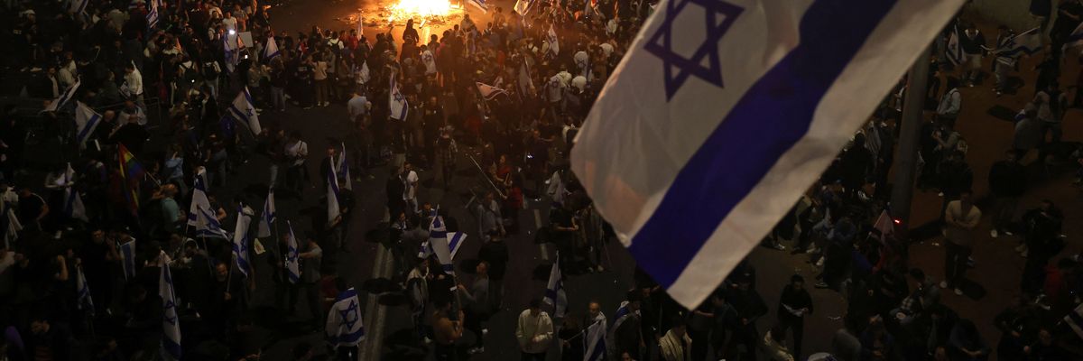 Israeli protesters block a road and hold national flags as they gather around a bonfire during a rally against the government's judicial reform in Tel Aviv on March 27, 2023.