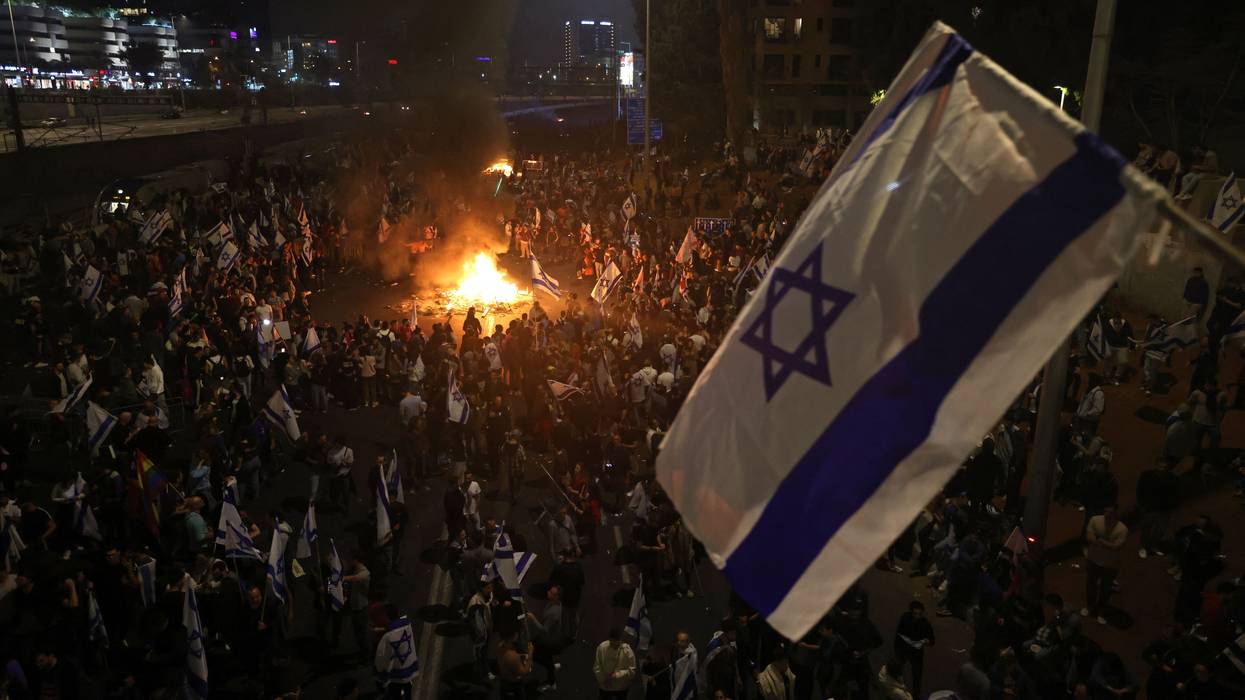Israeli protesters block a road and hold national flags as they gather around a bonfire during a rally against the government's judicial reform in Tel Aviv on March 27, 2023.