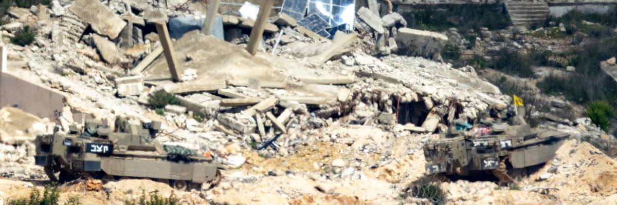 Israeli vehicle moves into Lebanon with rubble in the background.
