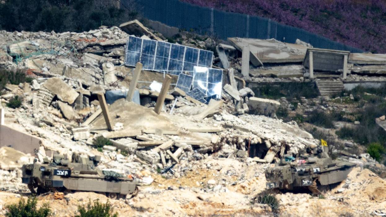 Israeli vehicle moves into Lebanon with rubble in the background.