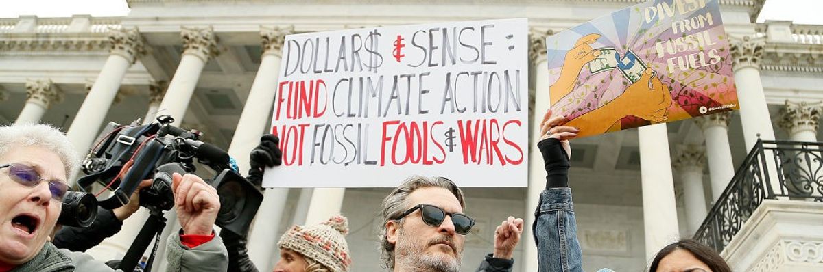 Joaquin Phoenix and other protesters stand on the Capitol steps with signs.