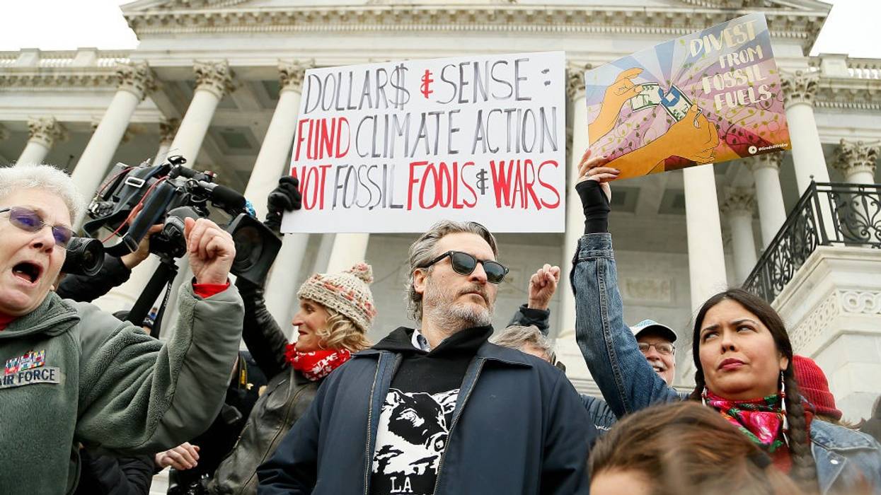 Joaquin Phoenix and other protesters stand on the Capitol steps with signs.