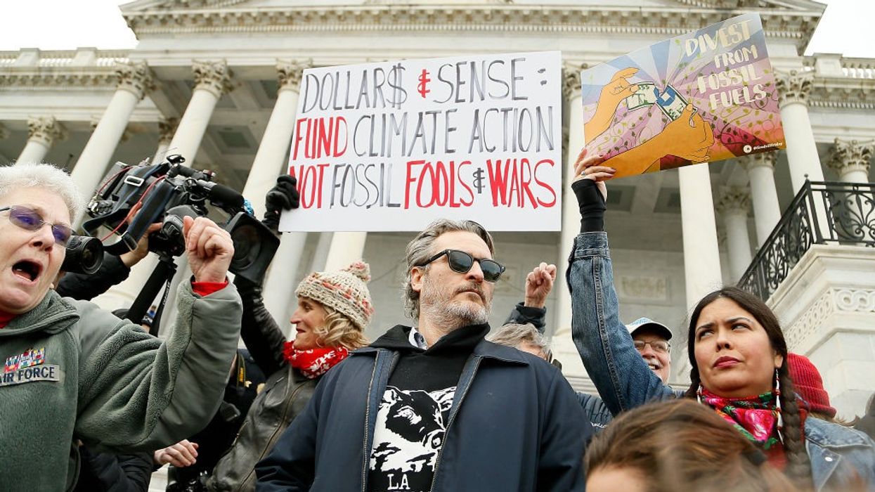 Joaquin Phoenix and other protesters stand on the Capitol steps with signs.