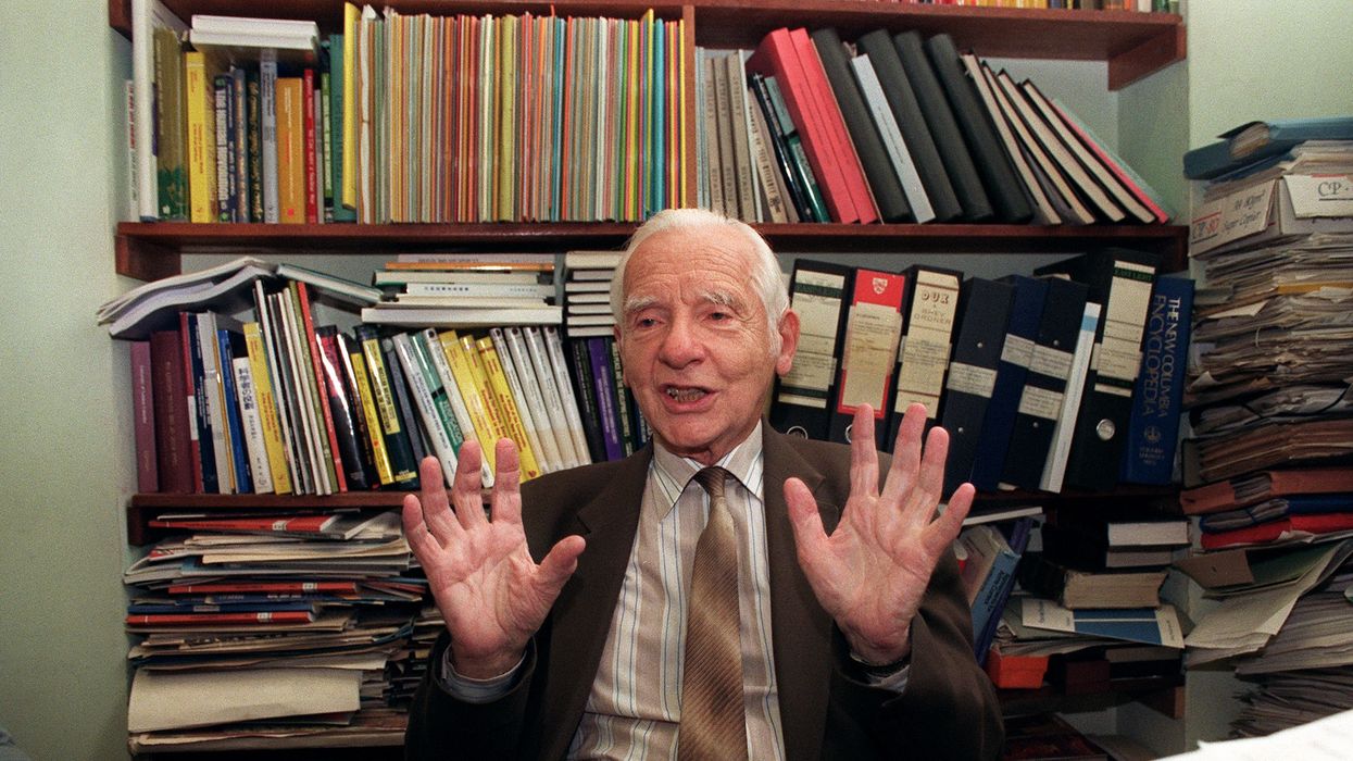 Joseph Rotblat with his hands raised sitting in front of books.