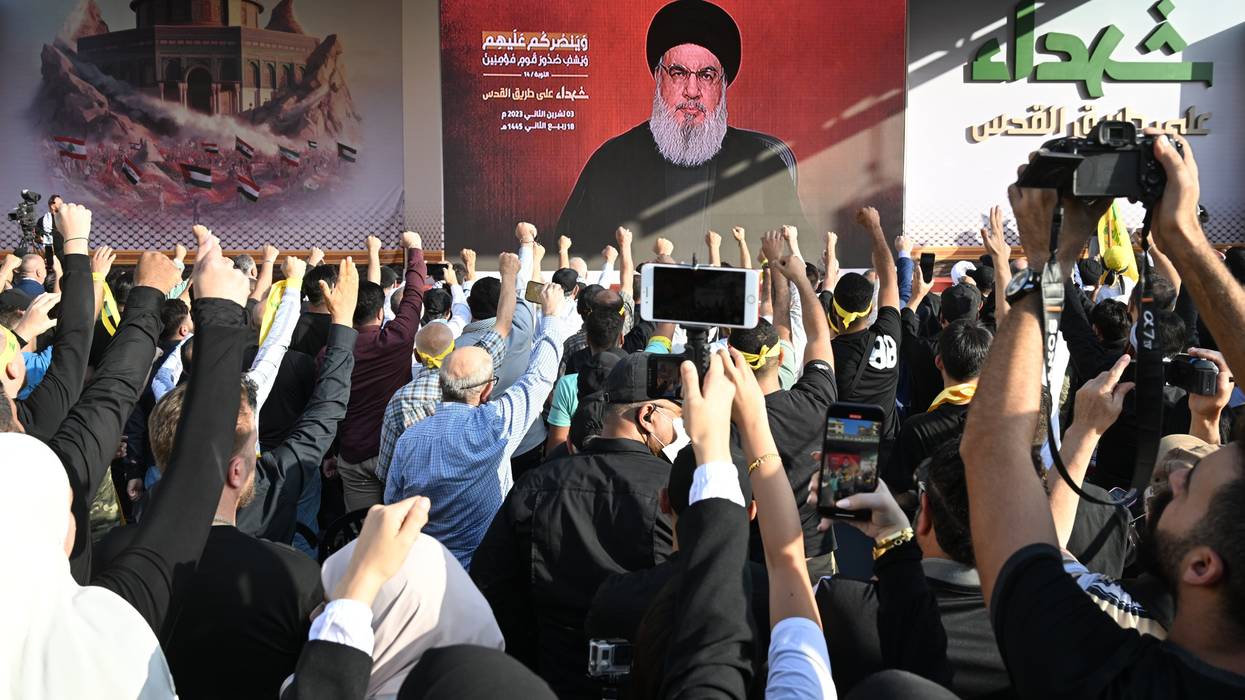Lebanese watch Hassan Nasrallah's speech on a massive video screen while raising their fists.