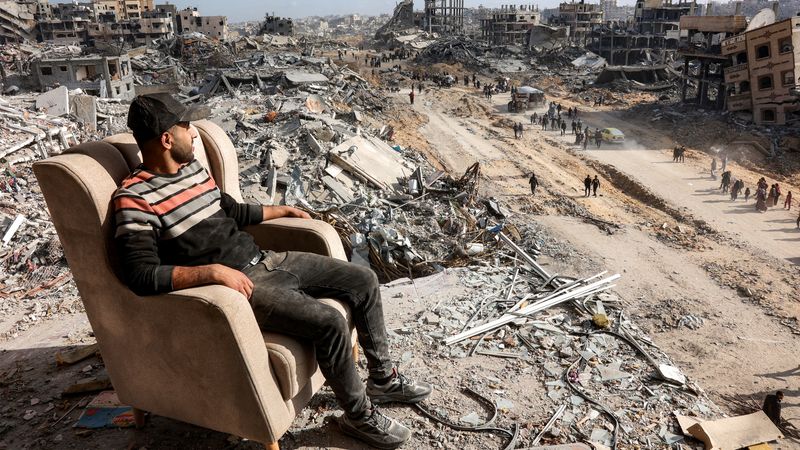 Man in Gaza sits in chair in front of rubble.