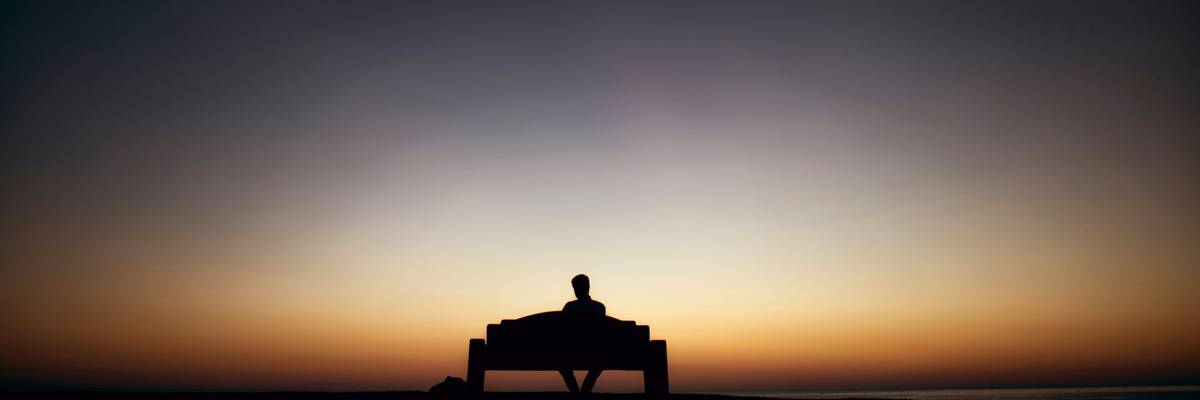Man on a bench faces sunset.
