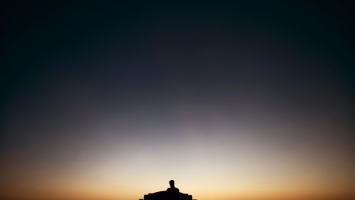 Man on a bench faces sunset.