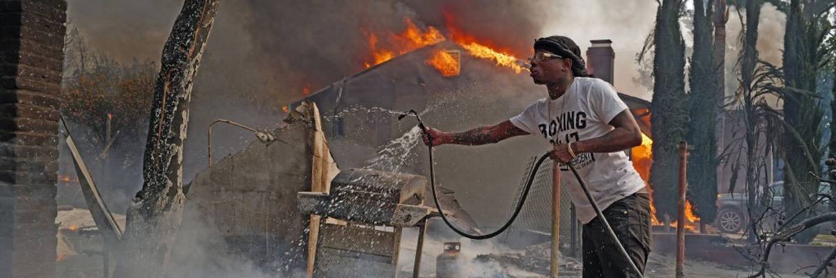 Man pours water from a hose on smoldering fire in Altadena